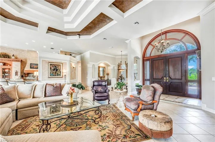 Tiled living room with coffered ceiling, a notable chandelier, decorative columns, crown molding, and a high ceiling
