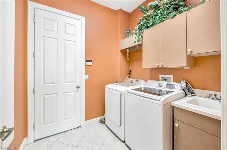 Laundry area with separate washer and dryer, cabinets, sink, and light tile patterned flooring