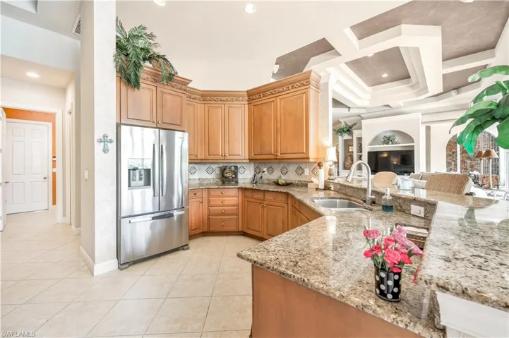 Kitchen featuring light stone countertops, sink, coffered ceiling, light tile patterned flooring, and stainless steel refrigerator with ice dispenser