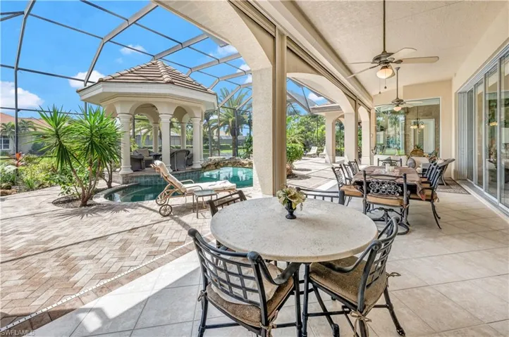 View of patio with glass enclosure, ceiling fan, a pool with hot tub, and a fire pit