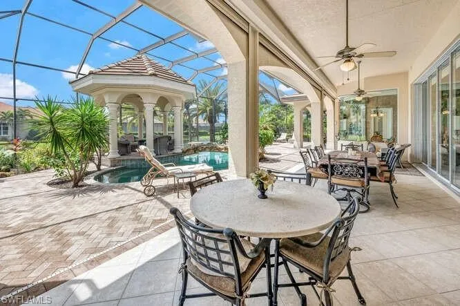 View of patio / terrace featuring glass enclosure, an outdoor fire pit, ceiling fan, and a pool with hot tub