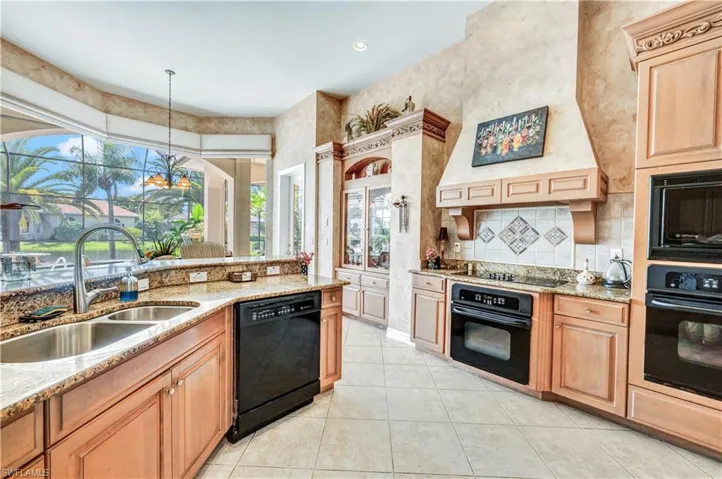 Kitchen featuring black appliances, sink, light stone countertops, and pendant lighting