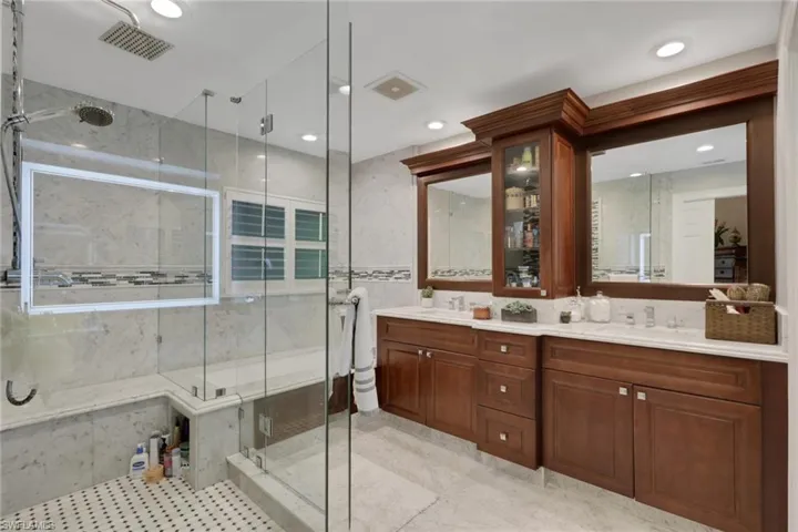 Bathroom with a marble finish shower, double vanity, tile walls, and recessed lighting