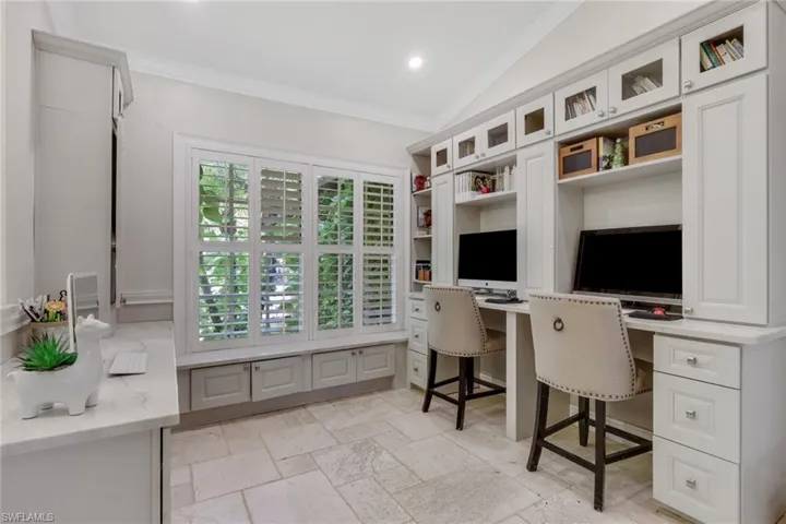 Office area featuring built in desk, ornamental molding, stone tile flooring, lofted ceiling, and recessed lighting