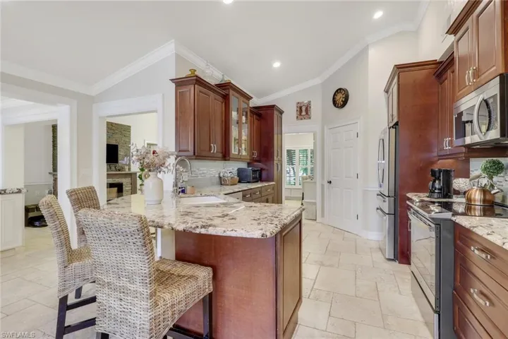 Kitchen with stainless steel appliances, backsplash, light stone countertops, glass insert cabinets, and a breakfast bar area