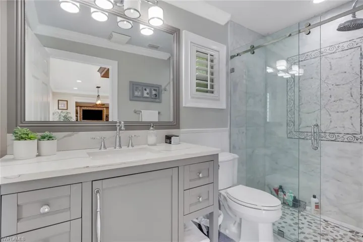Bathroom with ornamental molding, vanity, a marble finish shower, recessed lighting, and wainscoting