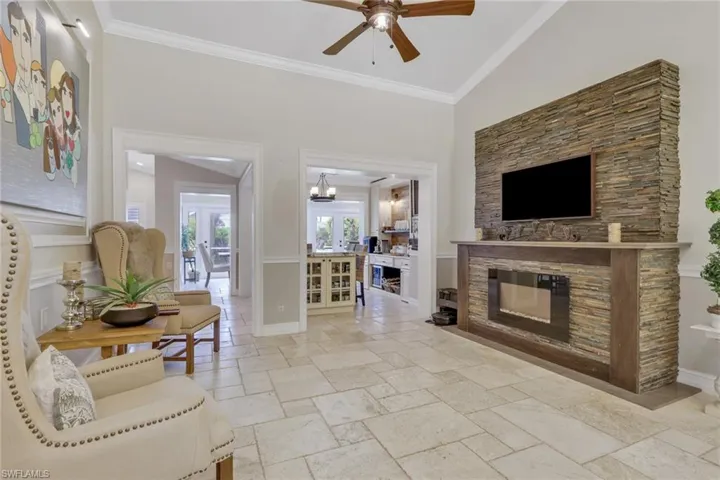 Living area with ornamental molding, stone tile floors, a fireplace, a ceiling fan, and a high ceiling
