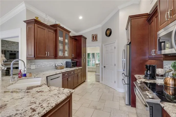 Kitchen with tasteful backsplash, stainless steel appliances, glass insert cabinets, light stone counters, and stone tile flooring