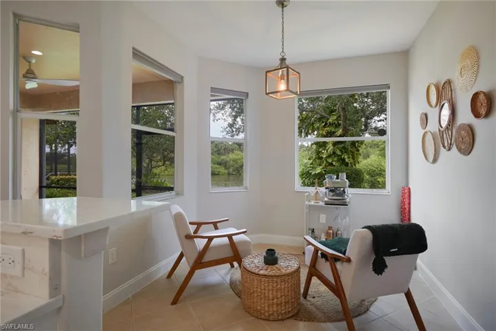 Light-filled interior space with multiple windows, a ceiling fan in the distance, a square pendant light fixture, and tile flooring