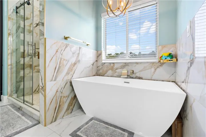 Full bathroom featuring tile walls, a chandelier, a marble finish shower, a freestanding bath, and marble tiled floors