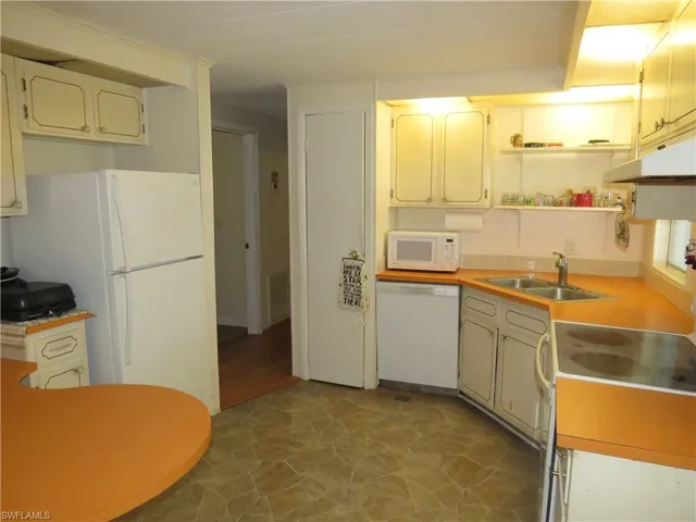 Kitchen featuring visible vents, under cabinet range hood, a sink, white appliances, and light countertops