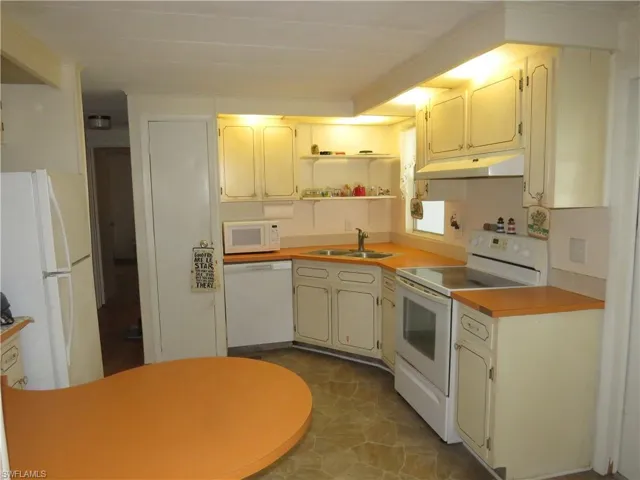 Kitchen with a sink, open shelves, under cabinet range hood, white appliances, and light countertops