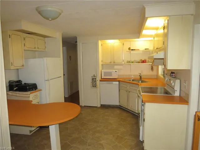 Kitchen with a sink, under cabinet range hood, light countertops, white appliances, and open shelves