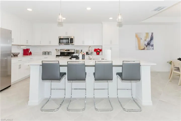 Kitchen with stainless steel appliances, light tile patterned flooring, an island with sink, light countertops, and white cabinets
