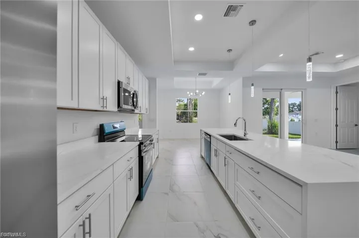 Kitchen with a raised ceiling, stainless steel appliances, white cabinets, light stone counters, and recessed lighting