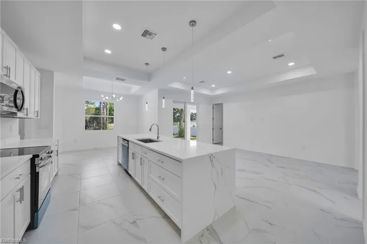 Kitchen featuring a raised ceiling, white cabinets, stainless steel appliances, light marble finish flooring, and light stone countertops