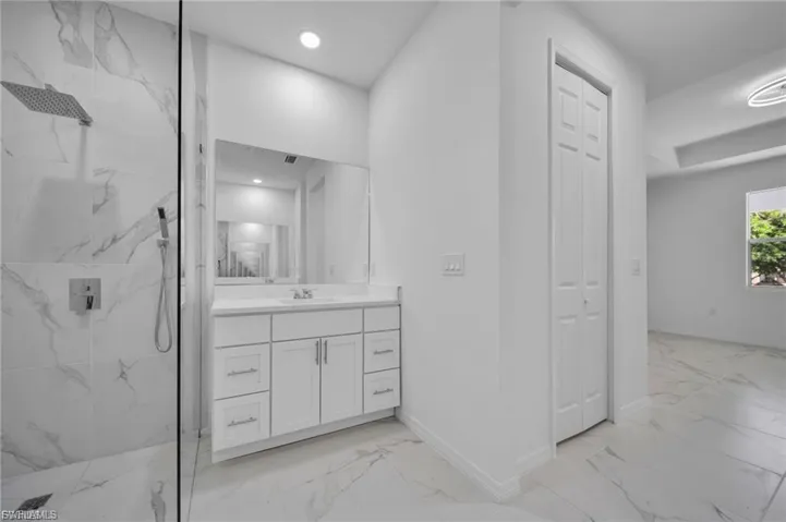 Bathroom featuring light marble finish floors, vanity, a marble finish shower, and a closet
