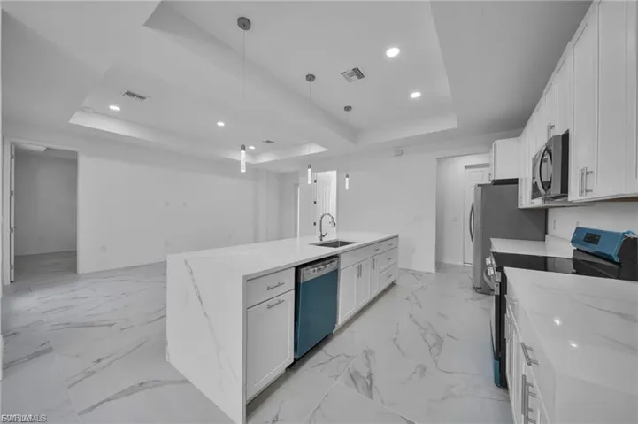 Kitchen featuring a tray ceiling, electric stove, white cabinets, light stone counters, and recessed lighting