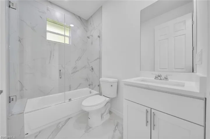 Full bath featuring vanity, combined bath / shower with glass door, and light marble finish flooring