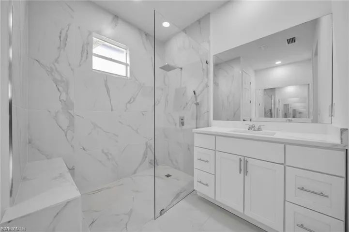 Bathroom featuring vanity, a marble finish shower, light marble finish floors, and recessed lighting