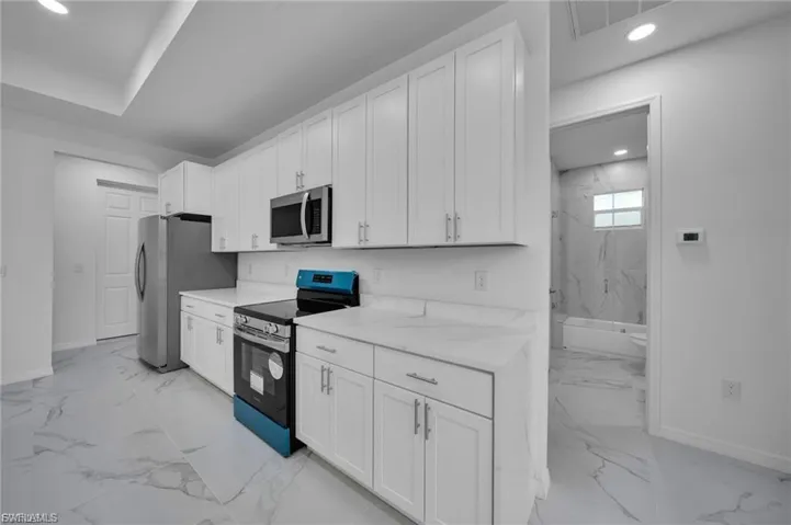 Kitchen with appliances with stainless steel finishes, recessed lighting, white cabinetry, light marble finish flooring, and light stone countertops
