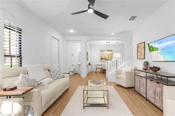 Living area with ceiling fan, light wood-style flooring, arched walkways, stairs, and a chandelier