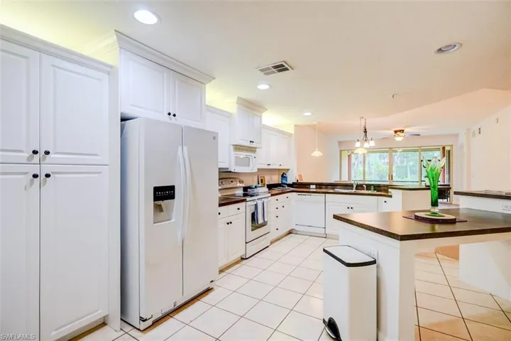 Kitchen featuring white appliances, white cabinetry, sink, and a breakfast bar