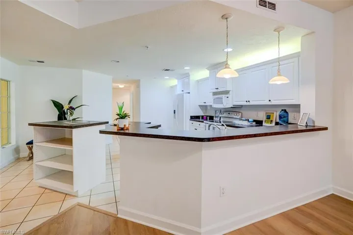 Kitchen featuring white cabinets, hanging light fixtures, kitchen peninsula, white appliances, and light wood-type flooring