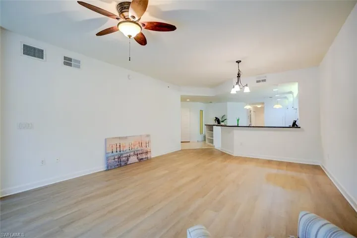 Unfurnished living room featuring ceiling fan with notable chandelier and light hardwood / wood-style floors