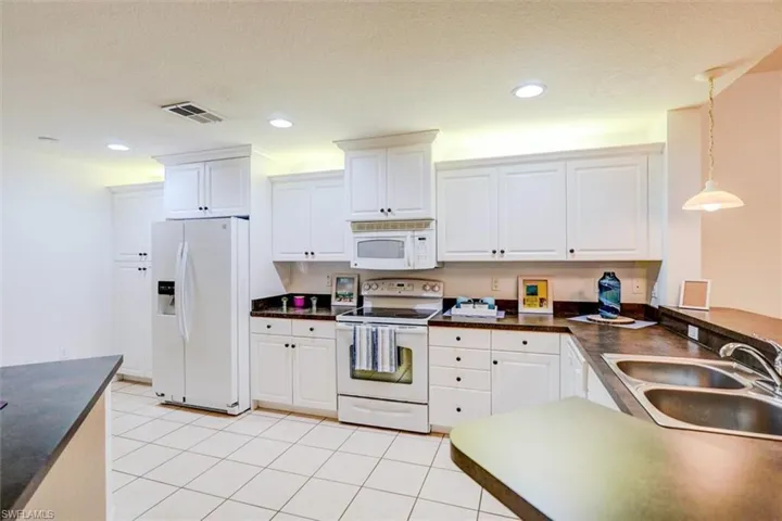 Kitchen with decorative light fixtures, sink, white appliances, and white cabinetry