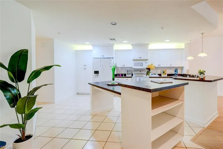 Kitchen with white cabinetry, hanging light fixtures, a kitchen island, white appliances, and light tile patterned floors