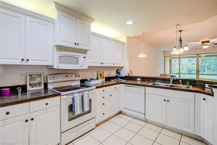 Kitchen featuring decorative light fixtures, white appliances, sink, and white cabinets