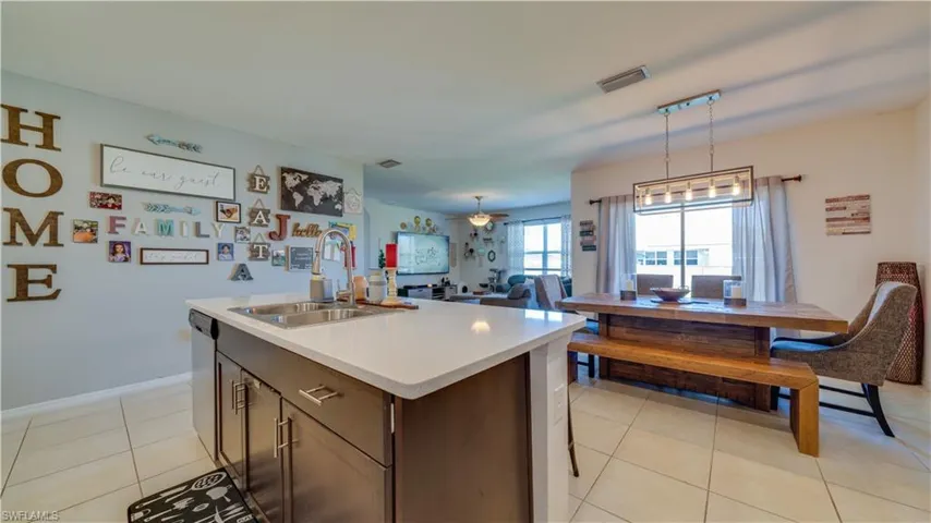 Kitchen featuring dark brown cabinets, open floor plan, an island with sink, light tile patterned flooring, and decorative light fixtures