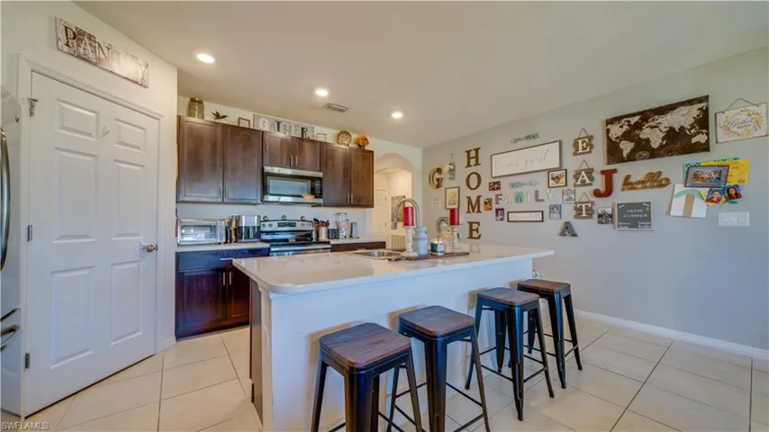 Kitchen featuring a kitchen breakfast bar, dark brown cabinetry, a kitchen island with sink, light tile patterned floors, and recessed lighting