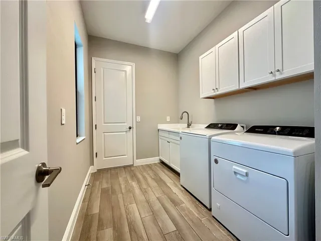 Washroom with washing machine and dryer, light hardwood / wood-style floors, sink, and cabinets