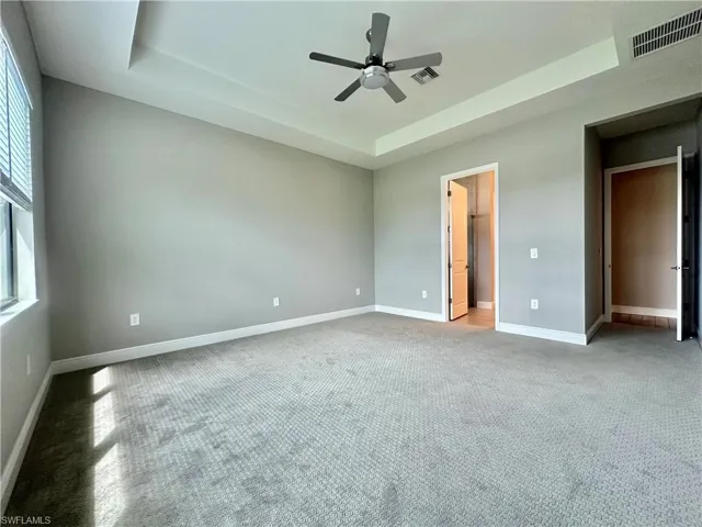 Unfurnished bedroom featuring light carpet, ensuite bath, ceiling fan, and a raised ceiling