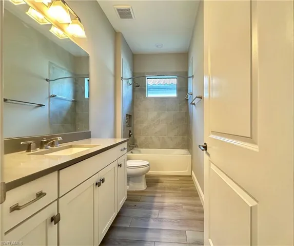 Full bathroom with tiled shower / bath combo, hardwood / wood-style flooring, vanity, and toilet
