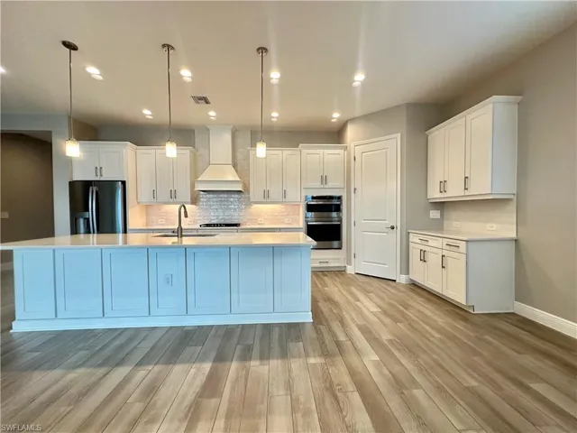Kitchen featuring custom range hood, pendant lighting, appliances with stainless steel finishes, and white cabinets
