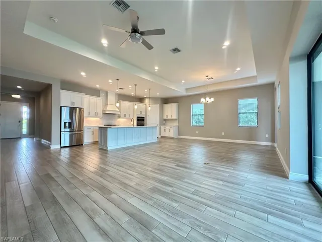Unfurnished living room featuring light hardwood / wood-style flooring, a tray ceiling, ceiling fan with notable chandelier, and sink