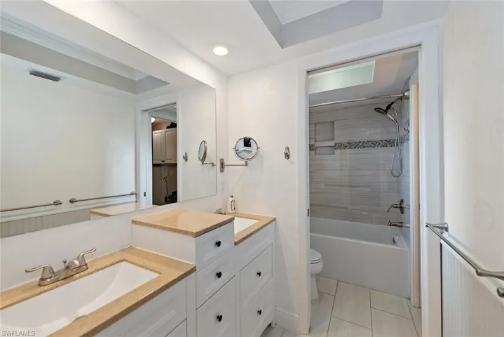 Full bath with shower / tub combination, double vanity, and light tile patterned flooring