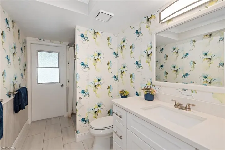 Bathroom with wallpapered walls, vanity, curtained shower, and light tile patterned flooring