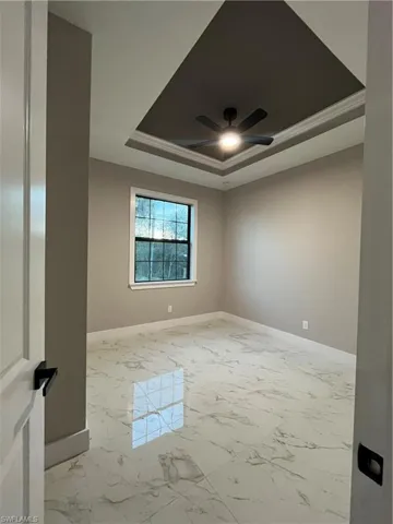 Unfurnished room featuring a raised ceiling, ceiling fan, and crown molding