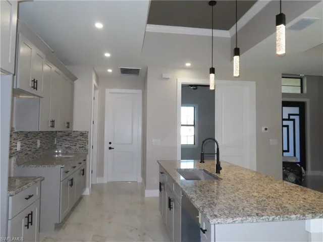 Kitchen featuring sink, light stone counters, a center island with sink, pendant lighting, and backsplash