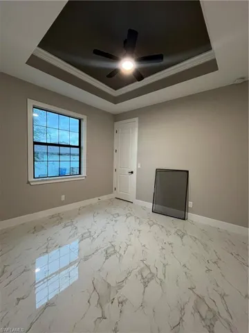 Empty room with ceiling fan, a raised ceiling, and crown molding