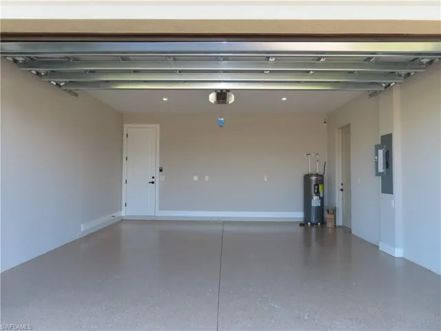 Garage with a garage door opener, electric panel, and electric water heater