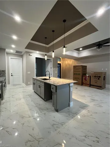 Kitchen with a kitchen island with sink, a raised ceiling, sink, gray cabinets, and decorative light fixtures