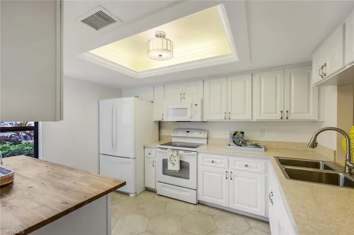 Kitchen with wood counters, white appliances, a tray ceiling, sink, and white cabinets