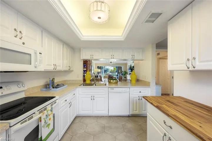Kitchen with white cabinetry, butcher block counters, white appliances, and sink