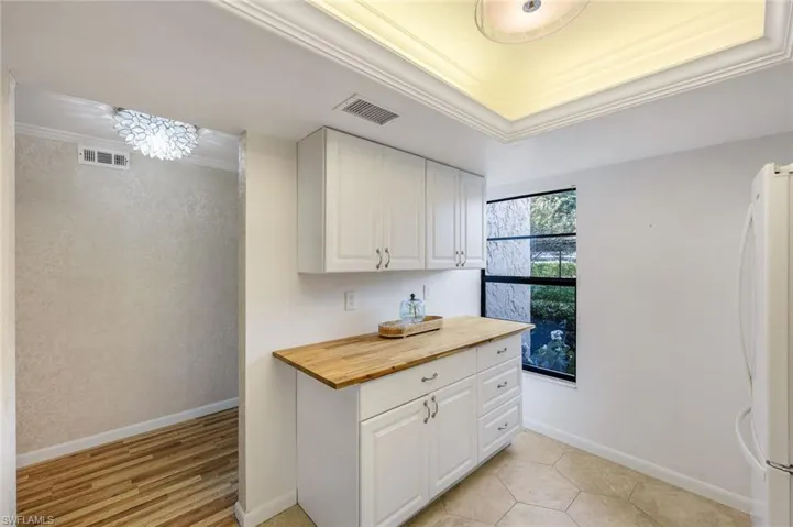 Kitchen featuring ornamental molding, a notable chandelier, white cabinets, white fridge, and butcher block counters