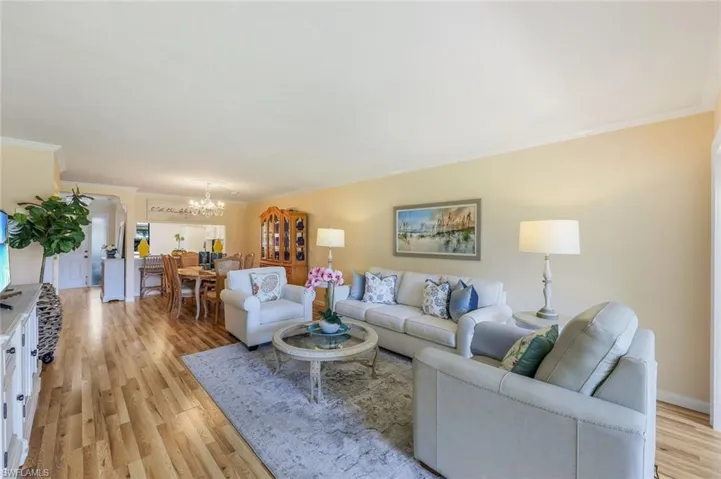 Living room with crown molding, a notable chandelier, and light wood-type flooring
